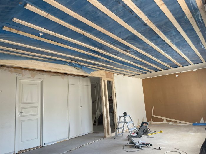 Renoveringsarbete med ny limträbalk installerad i taket, verktyg och stege på golv i ett halvfärdigt rum.