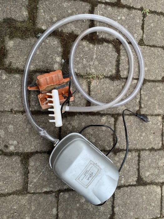 En dammfilter och pump anordning med en silverfärgad behållare, en grå slang och elektrisk kabel på marken.