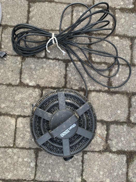 Ett svart Hozelock UV-filter för damm och en hoprullad svart sladd på gatsten.