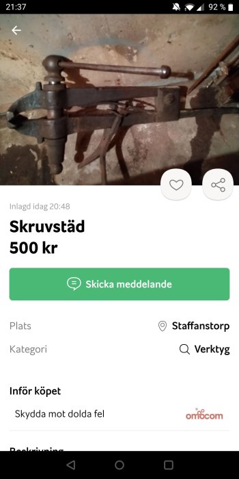 Gammal skruvstäd av metall mot en betongvägg, utannonserat för försäljning.