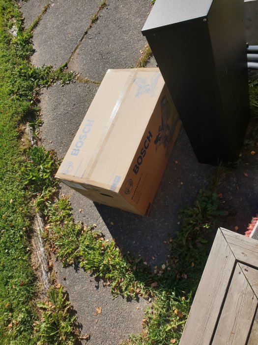 Ett paket från Bosch står på en gård nära en brevlåda i solljus.