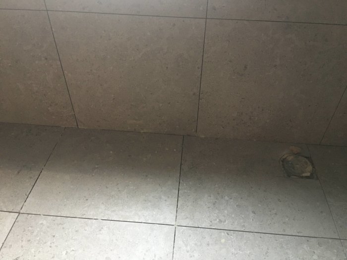60x60 kakelplattor på vägg och golv med synlig missmatchning vid golvbrunn.