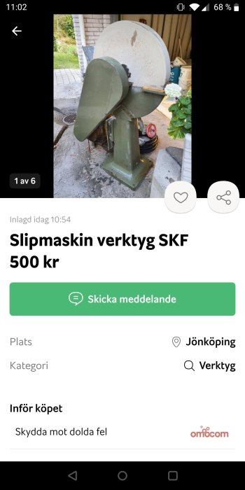 Gammal grön slipmaskin med stort vitt slipsten hjul placerad utomhus.