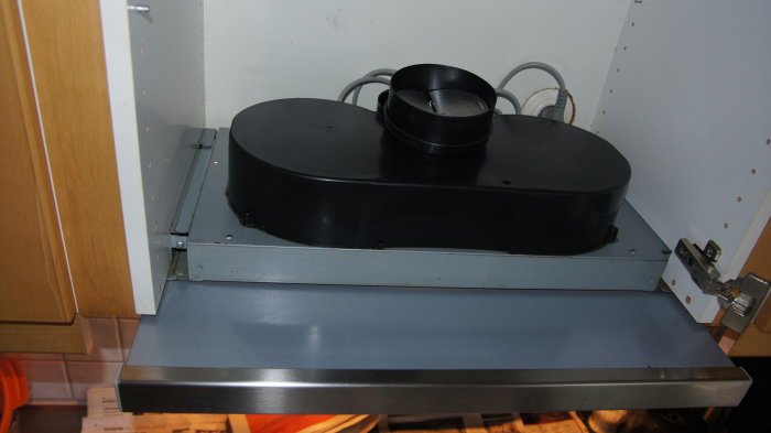 Svart kåpa på en Whirlpool köksfläkt monterad under köksskåp, i behov av demontering för rengöring.