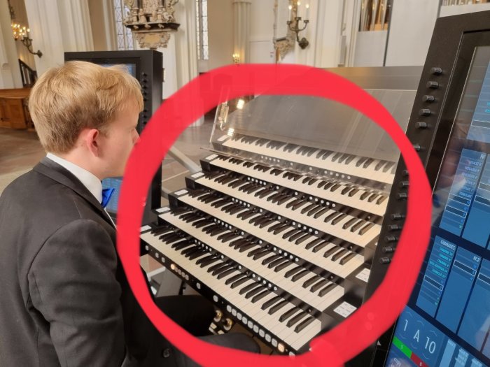 Person i kostym spelar på en kyrkorgel med flera manualer.