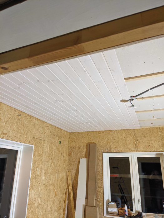 Nyinstallerat vitmålat paneltak i rum under renovering med OSB-skivor på väggarna.