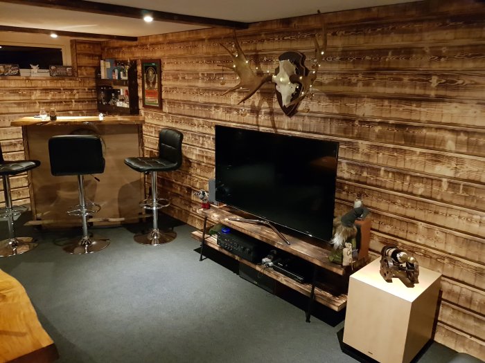 Inrett "Man cave" med bar, höga barstolar, stor TV och väggar klädda i träplank.