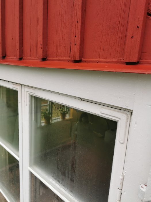 Nymålat fönsterbleck med röd färg på fasaden och ett vitt fönster under.