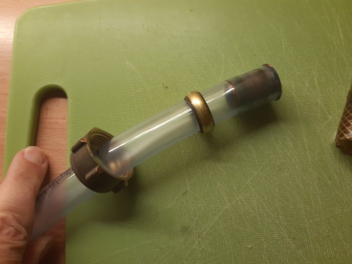 Transparent PVC-slang med kopplingar och gängtape sedd på ett skärbräde.