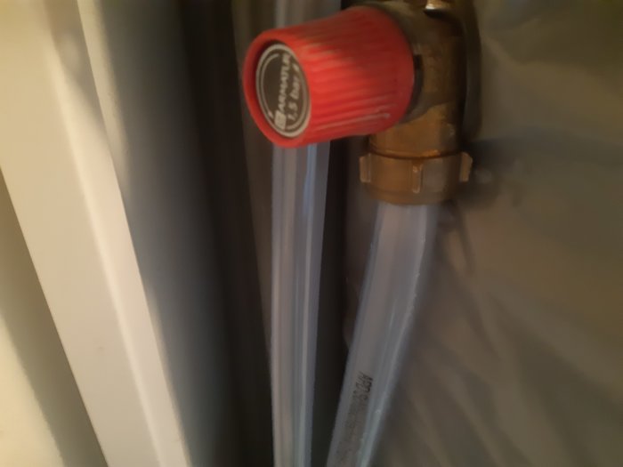 Ny genomskinlig PVC-slang ansluten till röd säkerhetsventil intill en varmvattenberedare.