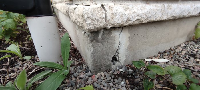 Skadad hörna på betongfundament med synliga sprickor och avfallande puts.
