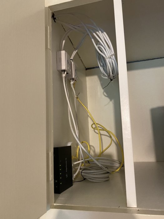 Organiserad nätverksutrustning med router och kablar i en garderob.