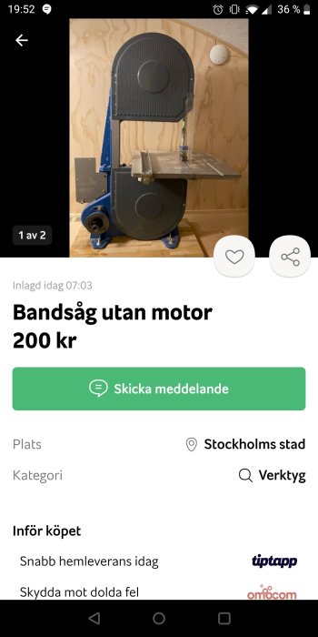 Blå och grå bandsåg utan motor på en arbetsbänk mot plywoodvägg.