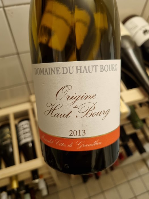 Närbild av en flaska vin Domaine du Haut Bourg Origine 2013 i ett vinställ.