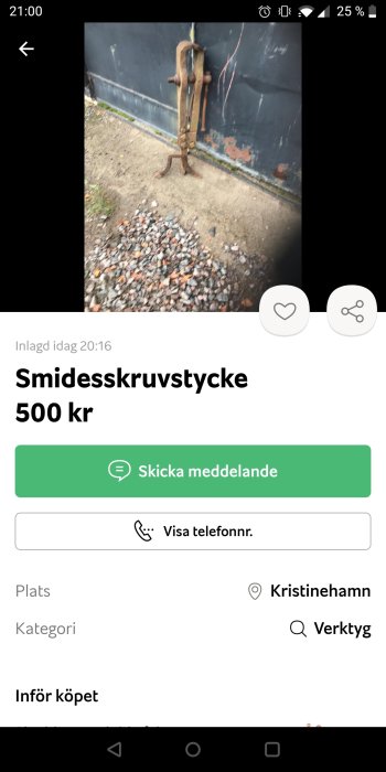 Gammalt smidesskruvstycke mot mörk bakgrund, rostigt, står på grus.