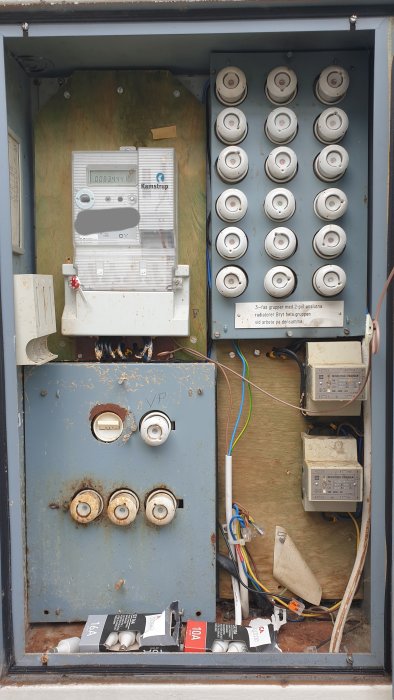 Äldre elskåp med elmätare, säkringar och några lösa kablar, tecken på oavslutat elektriskt arbete.