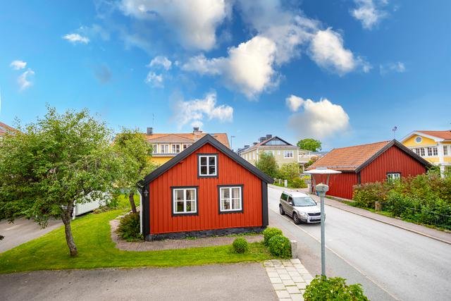 Rödmålad gammal stuga med vita knutar i Östhammar under en blå himmel med vita moln.