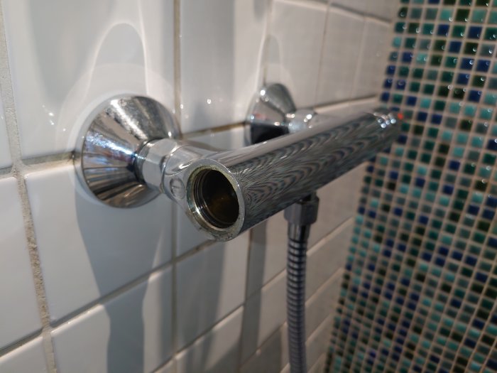Blandare utan flödesinsats monterad på vit kakelvägg med blå-grön mosaik i bakgrunden.