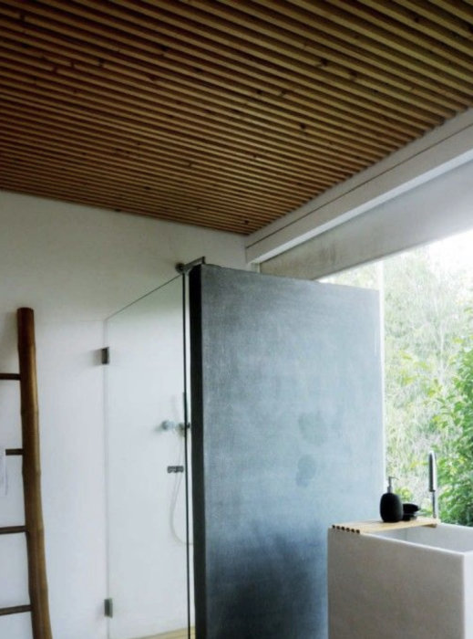 Modernt badrum med betongvägg, träinnertak och dusch bakom glasvägg.