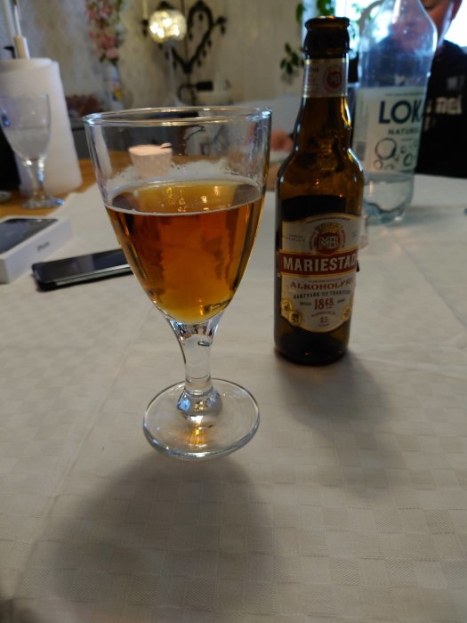 Ett glas med alkoholfri öl nära en öppnad Mariestads flaska på ett bord.