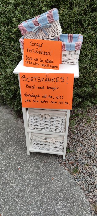 Vit byrå med flätade korgar och skyltar som säger "Bortskänkes! Korgar" och "Bortskänkes! Byrå med korgar".