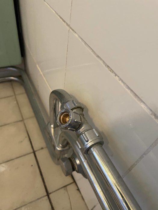 Rördel korrekt installerad vid vit kakelvägg och ansluten till vattenrör.