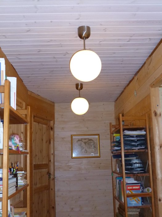 Vittvaxad träpanel i taket av ett rum med träväggar, en taklampa och inredning.