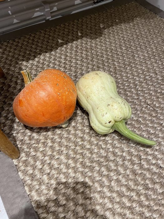 En orange och en vit pumpa på ett flätat underlag.