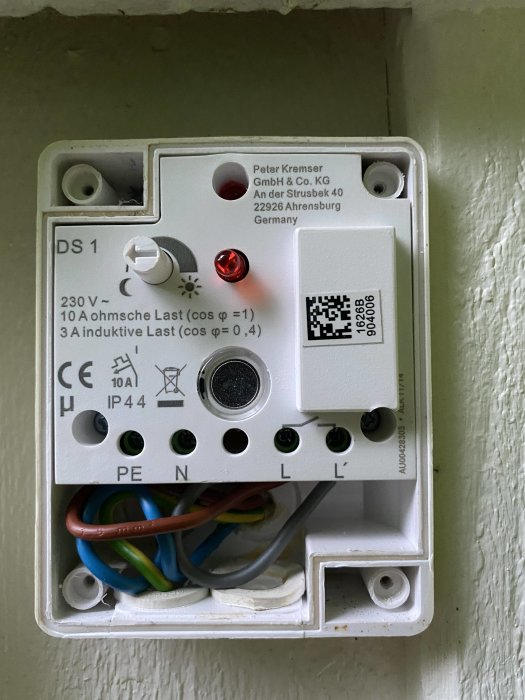 Öppen elektrisk installationsdosa med skymningsrelä, kablar anslutna, vred och ljussensor synlig.