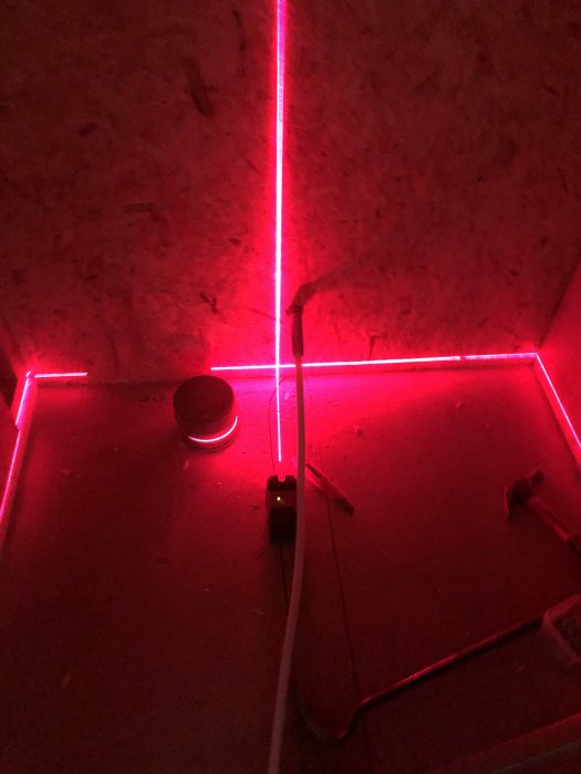 Röd lasernivell i arbete på en byggarbetsplats med synliga kablar och byggmaterial.