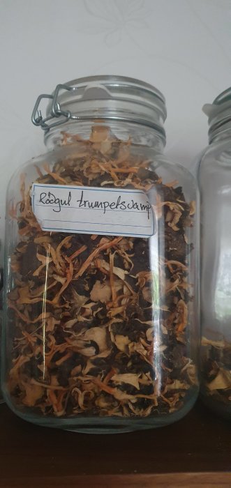 En glasburk fylld med torkade röda trumpetsvampar och en etikett som beskriver innehållet.