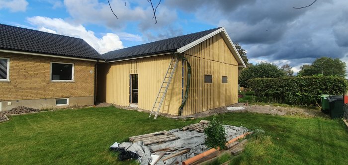 Ny målad trägavel på ett hus med en stege lutad mot väggen och byggmaterial utspridda på gräsmattan framför.