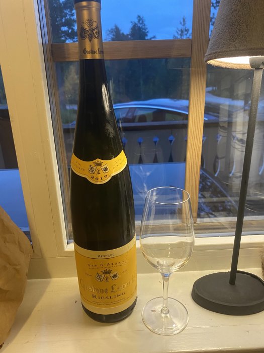 Flaska Gustave Lorentz Riesling vin och ett vinglas på ett fönsterbräde framför snötäckt utsikt.