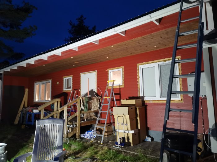 Nyligen installerade dimbara LED-spottar på underspikningen av ett rött hus under kvällshimmel, med stege och renoveringsmaterial framför.