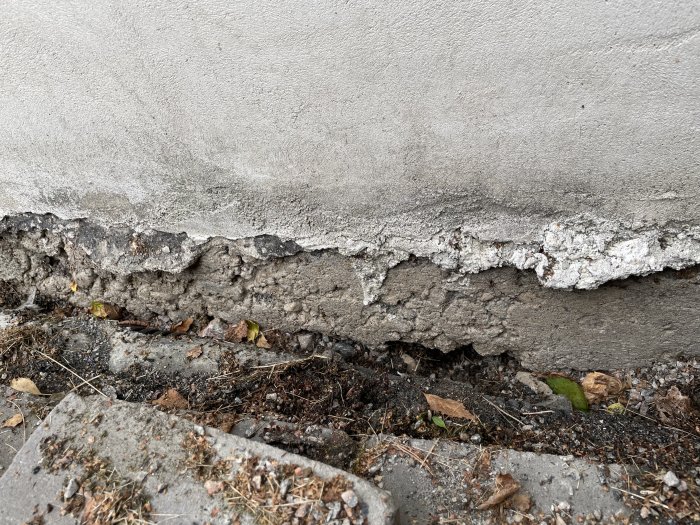 Erosionsskador vid husgrund med synligt dagvattenrör och svikande plattor.