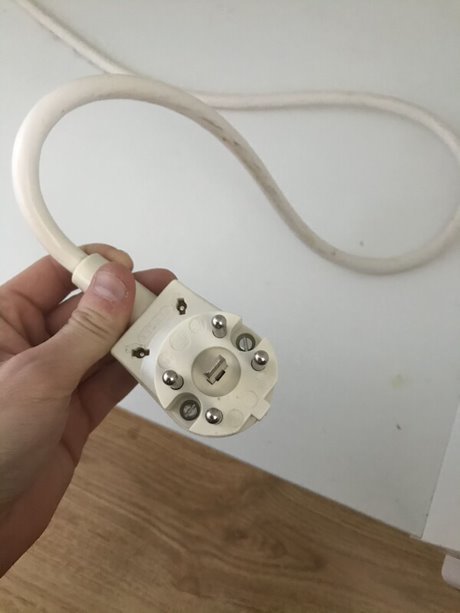 Hand håller en gammal spiskontakt med vit kabel, illustrerar fråga om installation av induktionshäll.