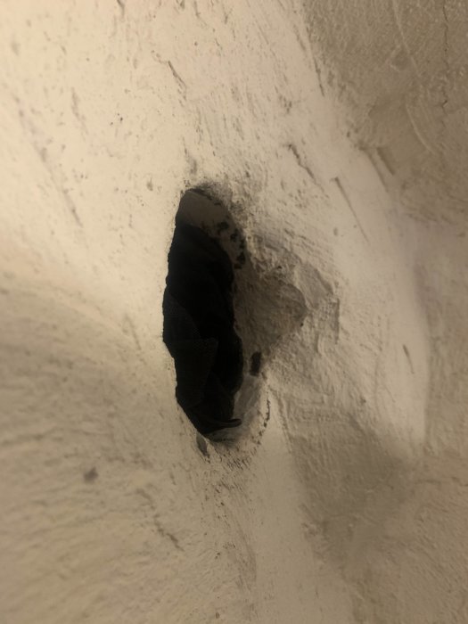 Ett öppet hål i en ojämn källarvägg där en kamin tidigare varit installerad, med synlig upphöjning intill.