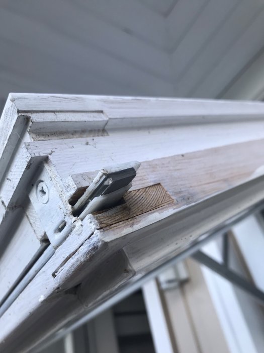 Närbild på ett gammalt vitmålat EPA-fönster med trasig plastdetalj vid låsmekanismen.
