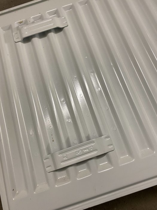 Baksidan av en vit radiator med befintliga plastkonsoler för väggmontering och 25cm cc märkning.