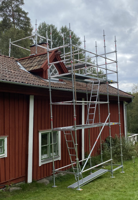 Ställning uppbyggd runt en röd stuga med tegeltak för arbete på skorstenen.