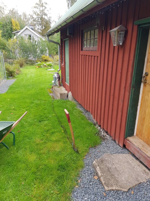 Ny rabatt vid snickarbod med spade, skottkärra och nyplanterade pioner i skymning.