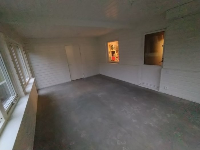 Tomt uterum med vita väggar och fönster, golv ej färdigställt, skymtar annat rum genom fönstret.