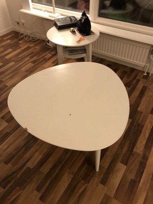 Ovalt vitt matbord på trägolv med en mindre rund sidobord och föremål på det.