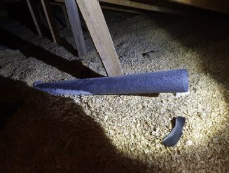 Avslutad ventilationskanal på en vind med synligt sug, belyst i strålkastarljus, omgiven av isoleringsmaterial.