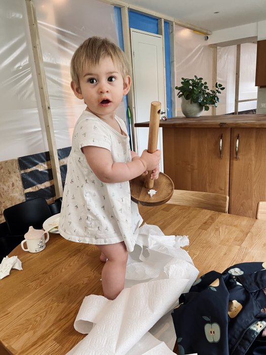 Barn står på bord med en träslev i handen under en köksrenovering.