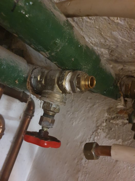 Ärgade rör och beslag inkluderande en röd ventilratt och en gängad koppling i en vägg, indikerande slitage och behov av byte.