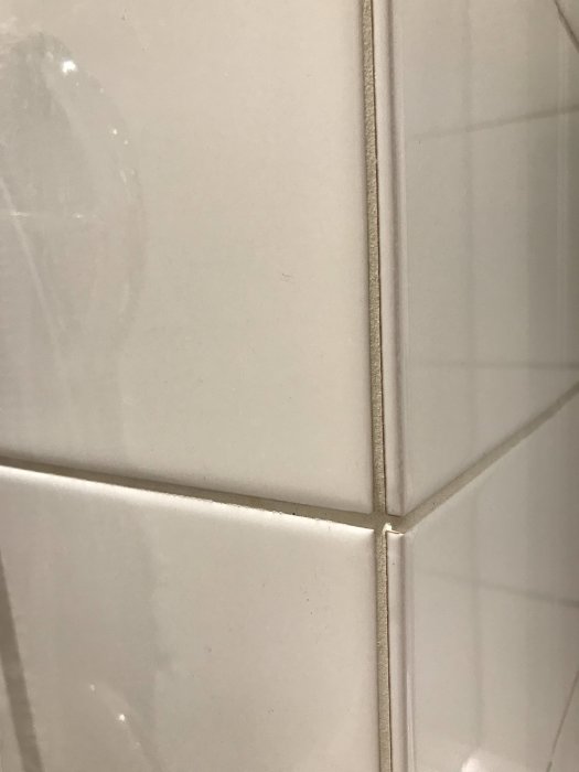 Vit kakelvägg med ljus fog och glaserad hörnkant för ett snyggt avslut.