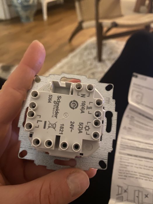 Hand håller en Schneider Exxact termostat bakifrån med synliga märkningar för N, L och 10(4)A för koppling av kablar.