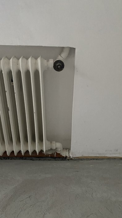 Vattenburen radiator kopplad till vägg med synlig ventil och röranslutning i rum under renovering.