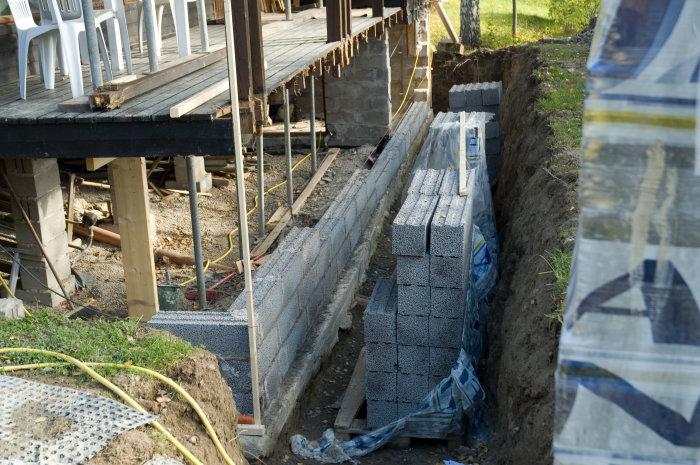 Grundmurning med armeringsjärn, platonmatta och betongblock vid husgrund under konstruktion.